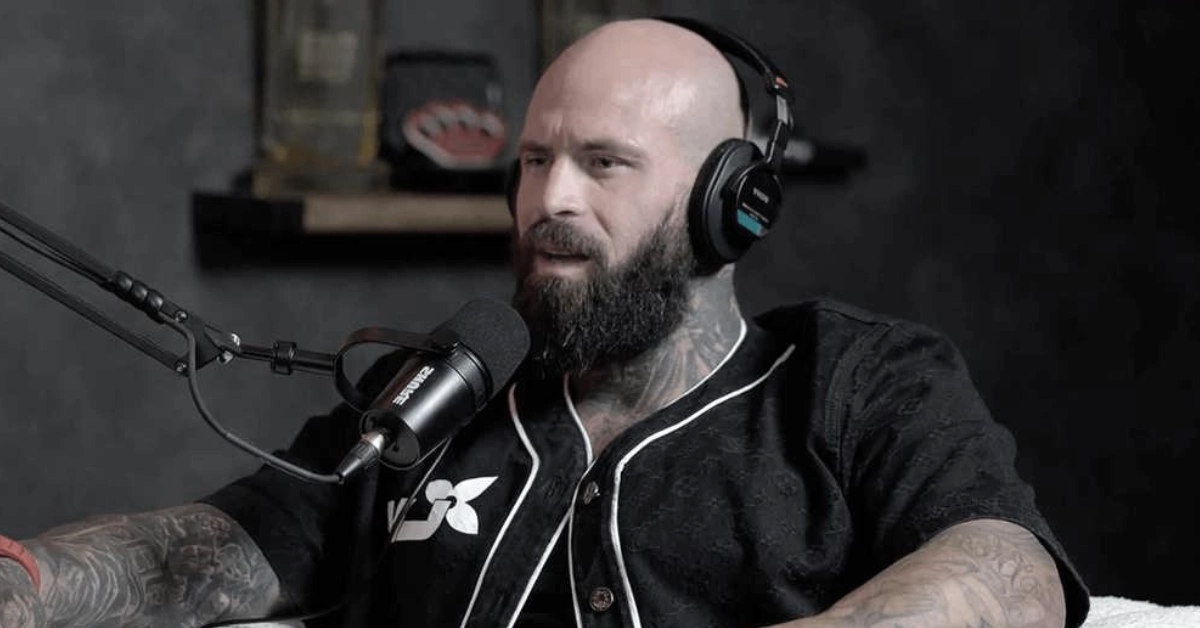 Wes Watson recording a podcast with headphones, showcasing his tattoos and beard while discussing his fitness empire and wealth journey from prison to entrepreneurship.