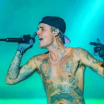 Justin Bieber performing shirtless on stage with tattoos visible, contributing to his estimated $300 million net worth through concerts that earn him up to $1 million per show.