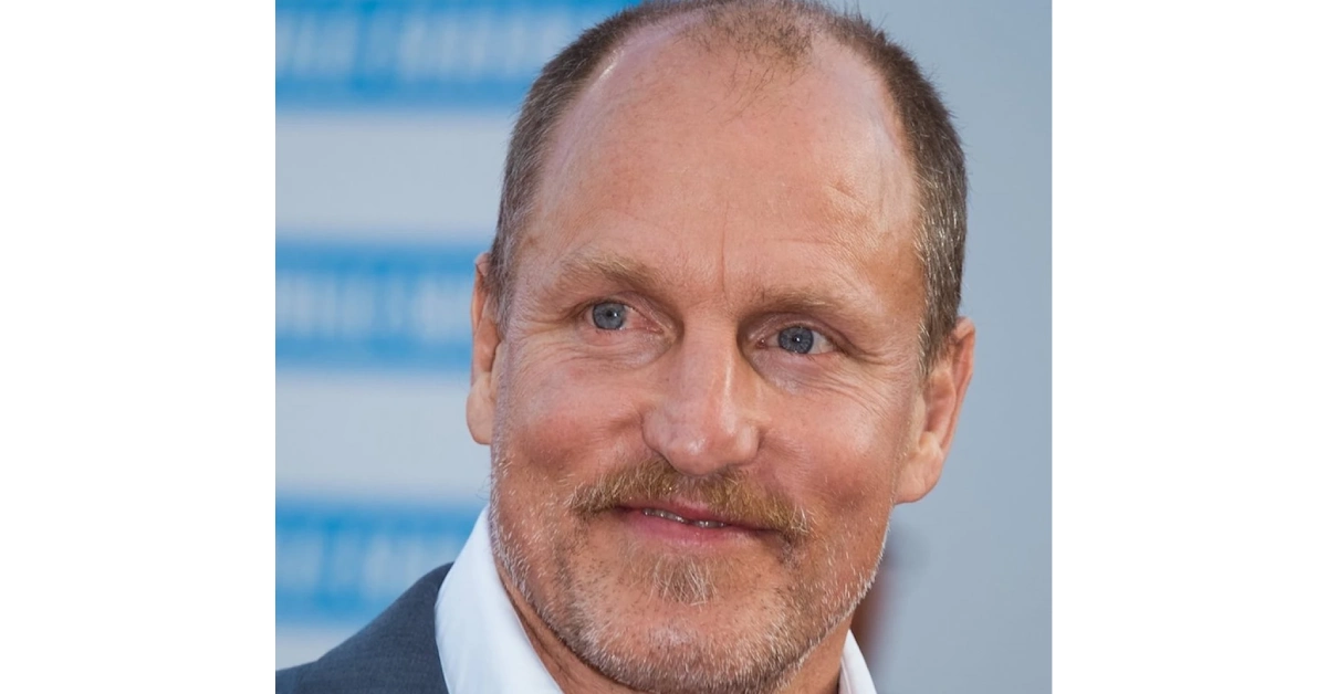 Woody Harrelson smiling in suit with blue background - actor with $70 million net worth
