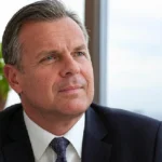 "Professional businessman in suit looking thoughtful in office setting, representing Door Loop's leadership and growing net worth"