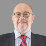 Mehmet Behçet Piker in business attire with glasses and red striped tie, former Sabancı Holding executive with estimated net worth between $150-200 million